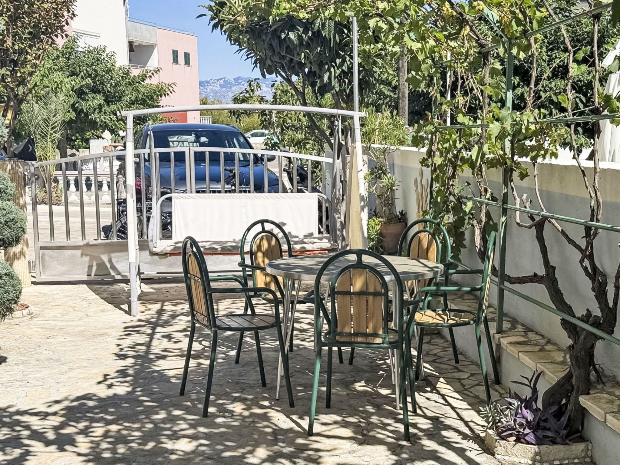 An outdoor seating area with tables and chairs, a covered table, and a vehicle parked behind a metal gate.