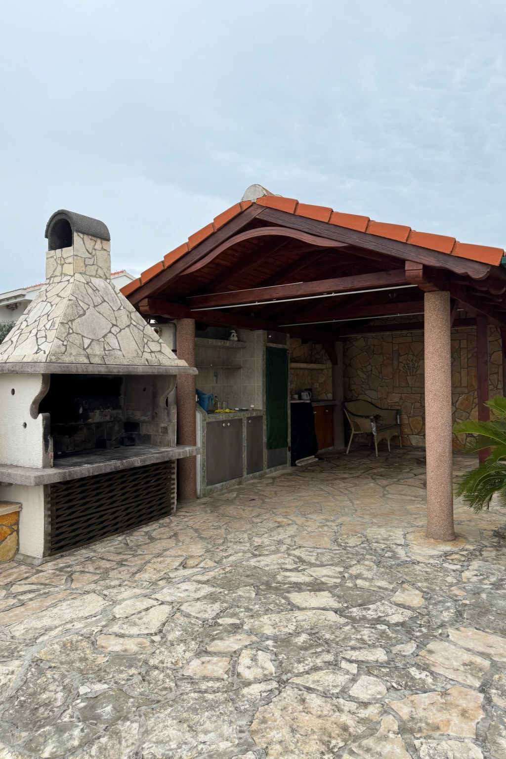 Eine Terrasse aus Stein mit einem Steingrill und einem überdachten Sitzbereich.