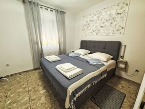 Een slaapkamer met een bed, gordijnen, een kunstwerk aan de muur en een betegelde vloer.