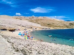 A beach with clear blue water, sandy shore, and a few umbrellas. - für 2 Personen ca. 25 m² in Zubovici, Adriaküste Kroatien (Kroatische Inse by Interhome (Pag/Zubovići)