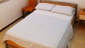 Ein Schlafzimmer mit einem Bett, einem orangefarbenen Sessel, einem Nachttisch und einem Fenster.