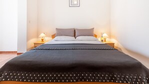 Un lit bien fait, recouvert d’une couverture foncée, deux tables de chevet avec des lampes et un tableau encadré au mur.