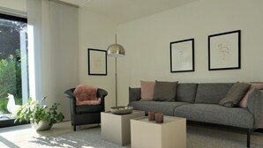 En moderne stue med en grå sofa, en sort lænestol og to firkantede sofaborde. Væggen er pyntet med billeder, og der står en høj gulvlampe.
