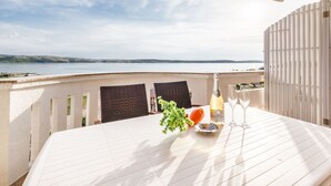Mesa para dos con una botella de champán, copas y un bol de frutas en una terraza con vistas al agua.