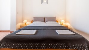 Una cama bien tendida con una manta oscura y almohadas, dos lámparas de noche y un cuadro en la pared.