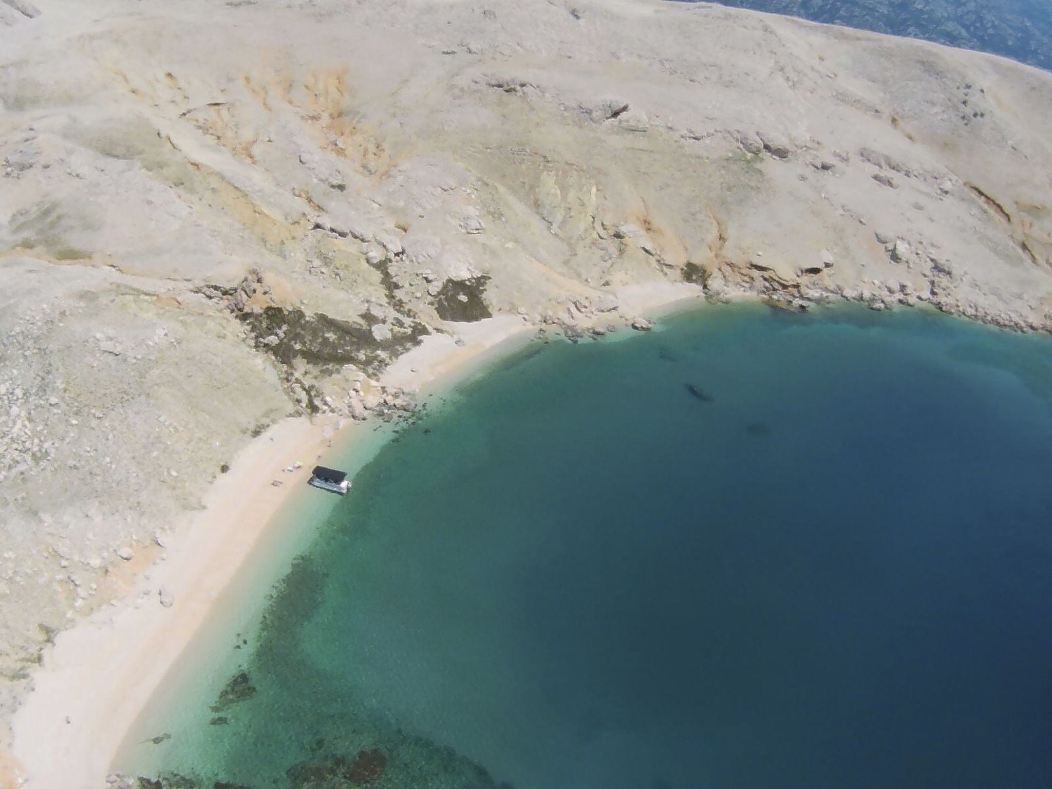 Luchtbeeld van een kustgebied met een helder strand en een klein bootje dichtbij de oever.