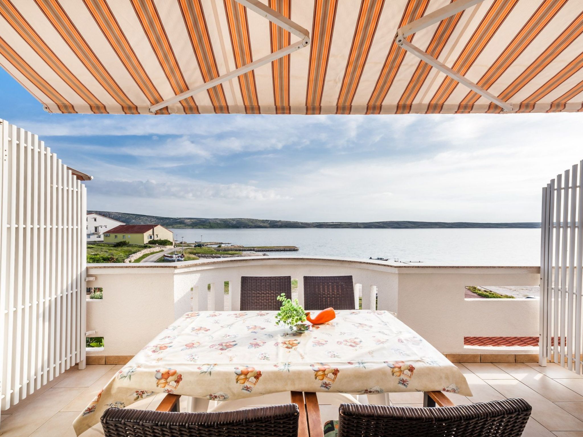 A terrace with a table and chairs, overlooking a body of water and distant landscape.