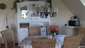 Un'area pranzo con sedie in vimini, un mobile bianco con vetrate, un lampadario e un vaso con fiori su un tavolo.