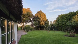 A well-maintained backyard with a swing set, a brick pathway, and a lawn. - Reetdachhaus Petra by Interhome (Helse)