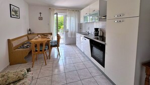 Una cucina compatta con mobili bianchi, una zona pranzo con una panca e sedie, e un tavolino con tazze e un cesto.