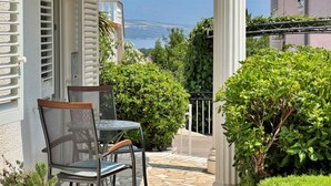 Una terrazza con tavolo e sedie, vista sul mare e un edificio con persiane.