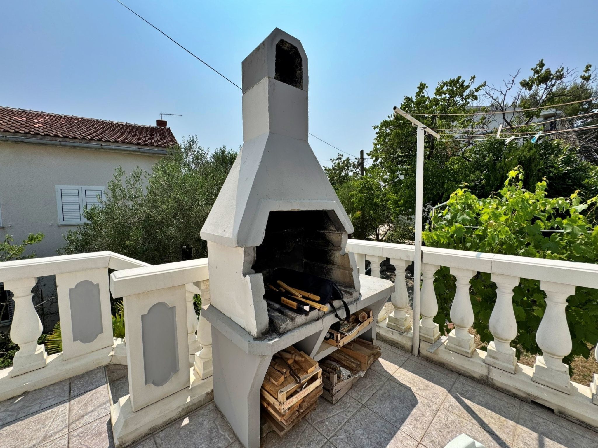 A stone-built outdoor grill with a chimney, surrounded by a white balustrade.