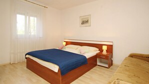 Ein Hotelzimmer mit einem hölzernen Bett, einem Nachttisch mit Lampe, einem Fenster mit Vorhängen und einem gerahmten Bild an der Wand.