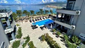 Une piscine sur le toit offrant une vue dégagée sur la mer, entourée de chaises longues et de plantes en pot.