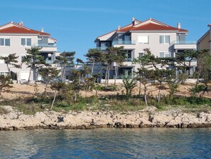 Un quartier résidentiel situé sur la côte, avec des maisons modernes à deux étages dotées de balcons et bordé d’une plage rocheuse.