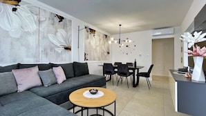 Een moderne woonkamer met een grijze modulaire bank, een ronde houten salontafel en een eethoek met een donkere tafel en stoelen.