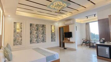 Habitación de hotel moderna con cama, escritorio, televisor y kitchenette.