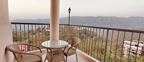 A balcony with a round glass table and wicker chairs, overlooking a mountainous landscape.