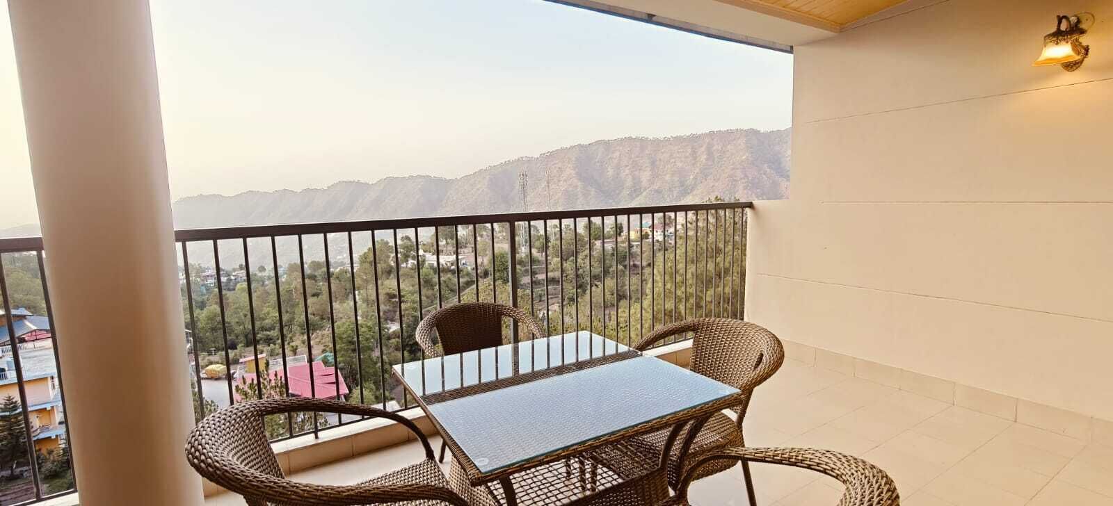 Ein Balkon mit Tisch und Stühlen, der Blick auf eine Berglandschaft freigibt.