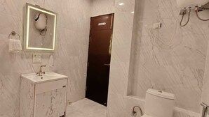 A bathroom with a marble wall, a sink with a mirror, a toilet, and a shower area.