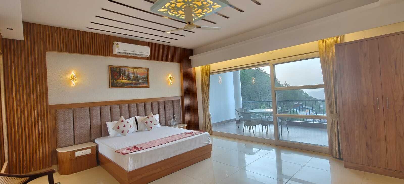 A bedroom with a large bed, a nightstand, a wall-mounted air conditioner, a painting, and a view of the outdoors through a sliding glass door.
