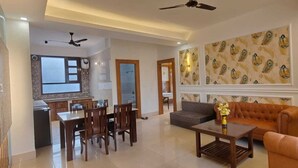 A living room with a sofa, dining table, chairs, and a kitchen area with a refrigerator and microwave.