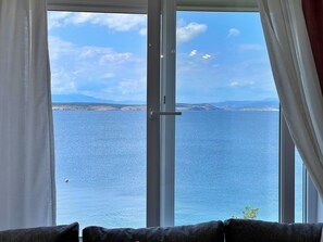 Quarto com uma grande janela que oferece vista para um mar calmo e terra distante.