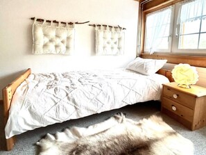 Une chambre à coucher avec un lit, une table de chevet, une fenêtre et un tapis en fourrure.