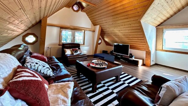 A cozy attic bedroom with a sloped ceiling, a large window, a leather sofa, a TV, and a fireplace. - Sonnige Maisonette by Interhome (Dicken)