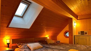 A cozy attic bedroom with a sloped ceiling, a skylight, a bed with a quilted cover, a bedside table, and a lamp. - Sonnige Maisonette by Interhome (Dicken)