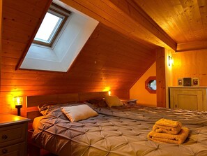 Ein gemütliches Schlafzimmer im Dachgeschoss mit schrägen Wänden, einem Oberlicht, einem Bett mit gesteppter Decke, einem Nachttisch und einer Lampe.