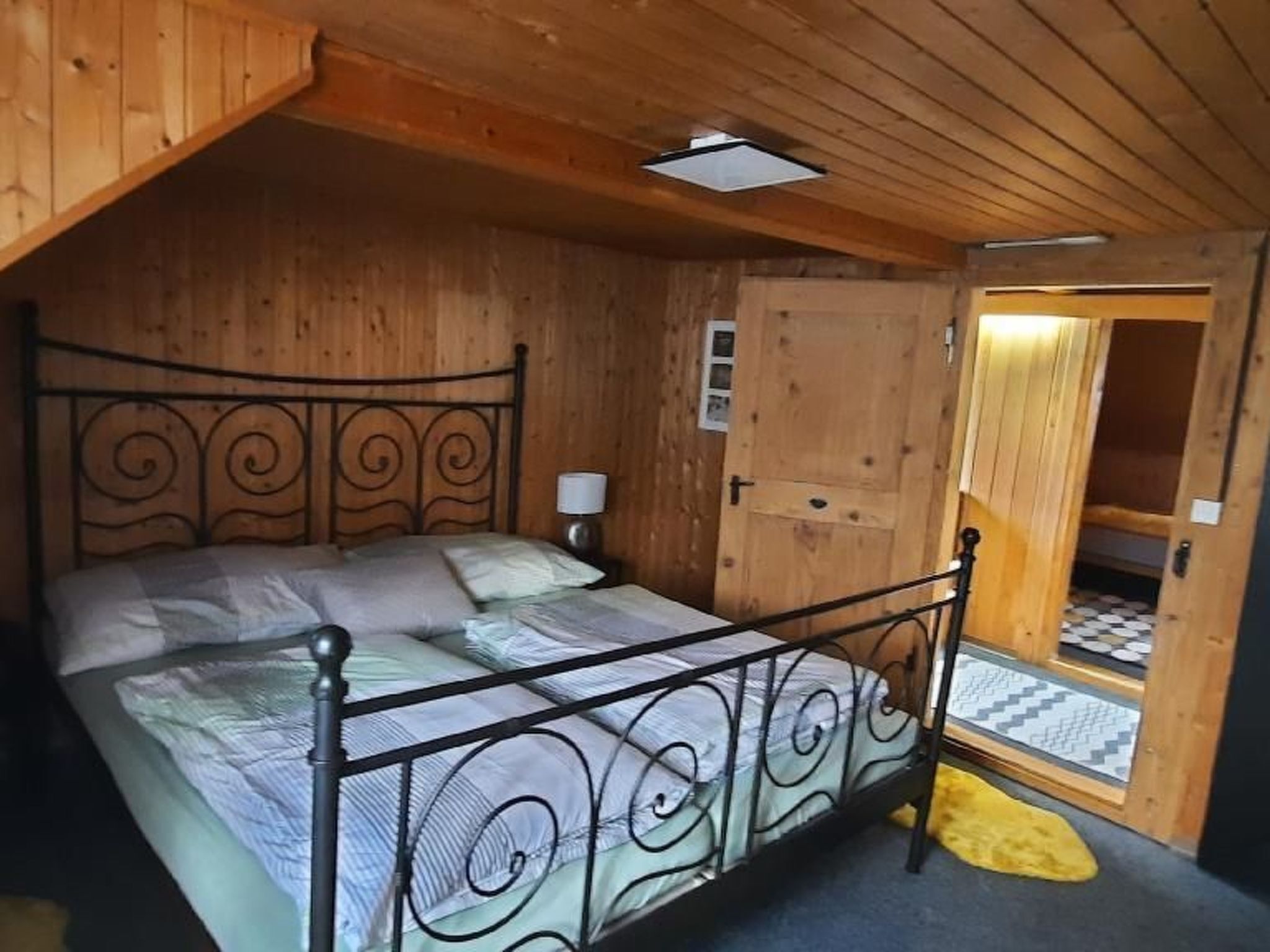 Una habitación de madera con una cama, una puerta y un ventanal pequeño.