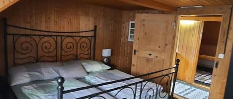Una habitación de madera con una cama, una puerta y un ventanal pequeño.