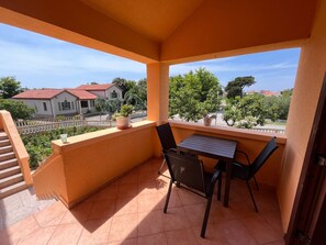 Ein Balkon mit Tisch und Stühlen, Blumentöpfen und Blick auf Häuser und Grünflächen.