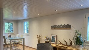 Moderni sisustus, jossa on lasinen ruokapöytä, mukava nojatuoli ja puinen kirjahylly.