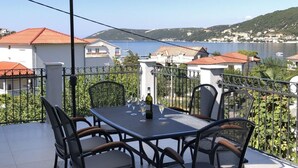 Eine Terrasse mit Tisch und Stühlen, einem großen Sonnenschirm und Blick auf eine Küstenstadt.