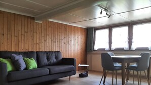 A room with a dark grey sofa, green and grey cushions, a round dining table with four chairs, wooden flooring, and a window with curtains. - auf dem Bauernhof by Interhome (Lütisburg Station)