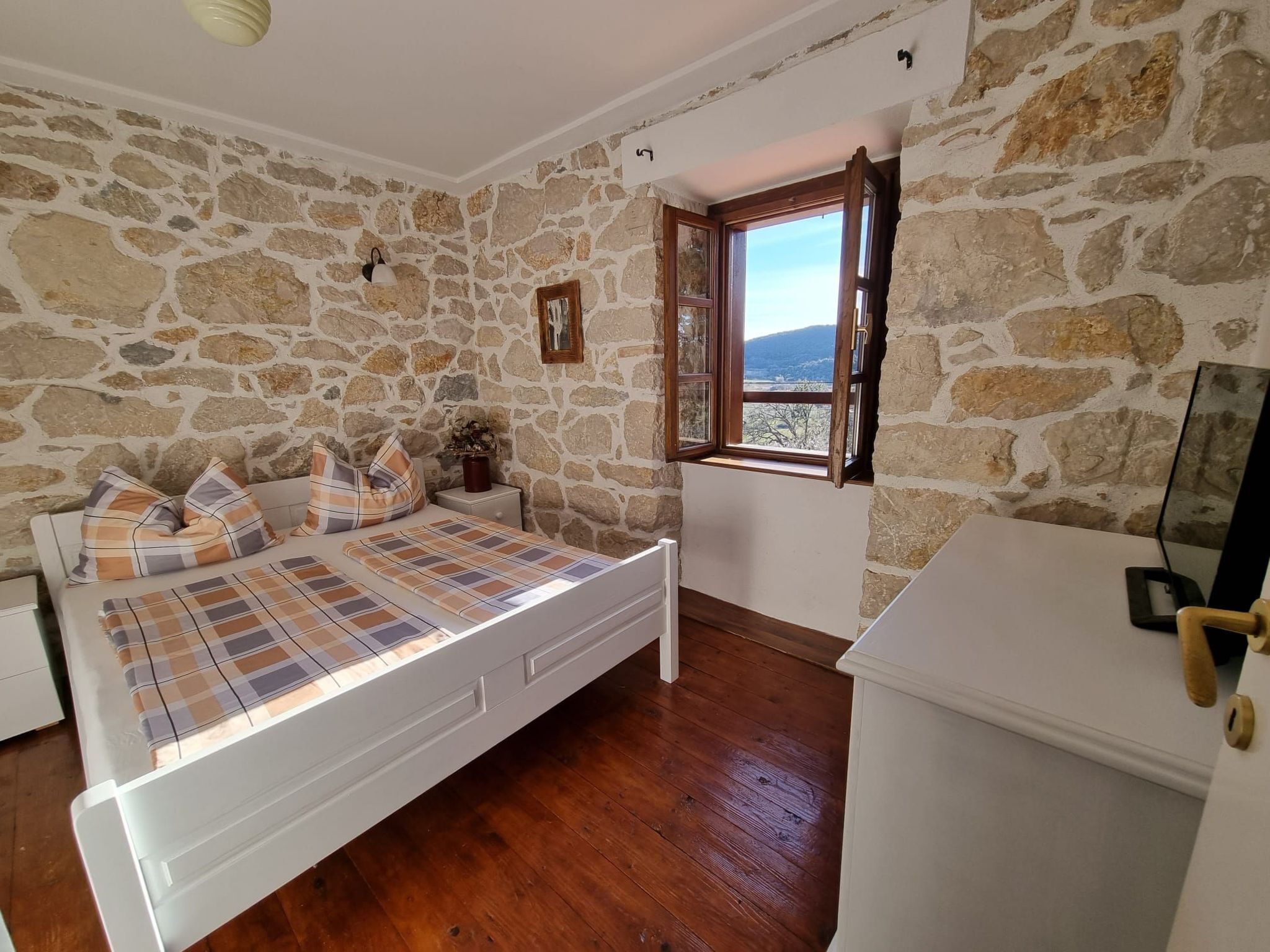 Un dormitorio con pared de piedra, una cama con ropa de cama escocesa, suelo de madera y una ventana con vistas.