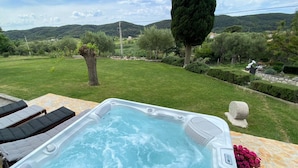 A hot tub with a stone table and lounge chairs in a backyard with a view of hills. - Tolles Ferienhaus in Supetarska Draga mit Garten by Interhome (Rab/Supetarska Draga)