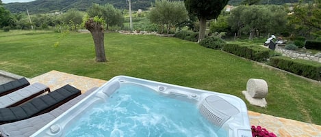 A hot tub with a stone table and lounge chairs in a backyard with a view of hills.