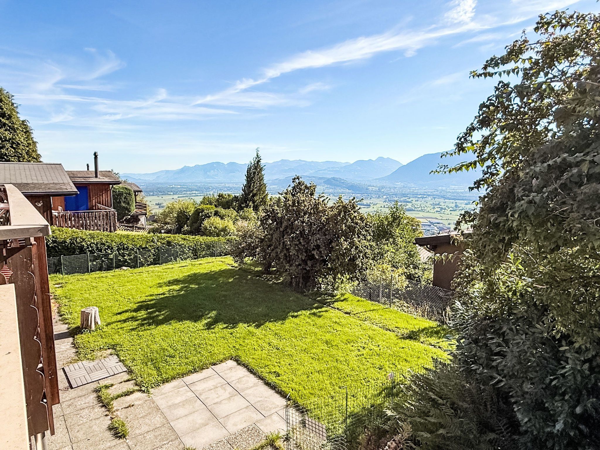 A residential property with a well-maintained lawn, a wooden deck, and a view of distant mountains.