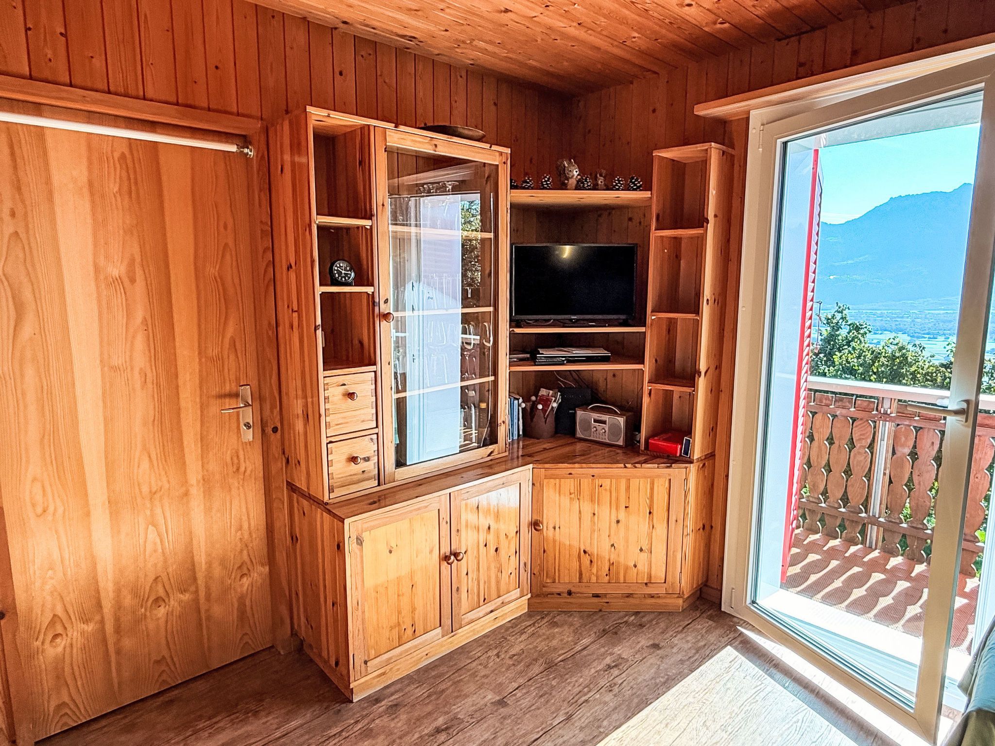 A wooden interior with a television, cabinets, and a sliding glass door to a balcony.