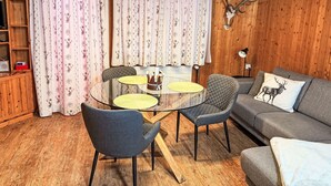 Een gezellige kamer met houten plafond, een rond glazen tafel met stoelen, een grijze bank en een decoratie van een hertengewei.
