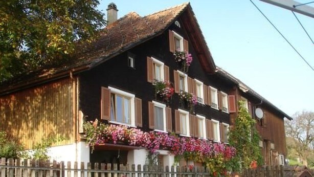 Un chalé tradicional con fachada de madera, múltiples ventanas con contraventanas y un balcón decorado con flores.