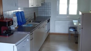 Una cocina compacta con armarios blancos, horno integrado, lavamanos y ventana que proporciona luz natural.