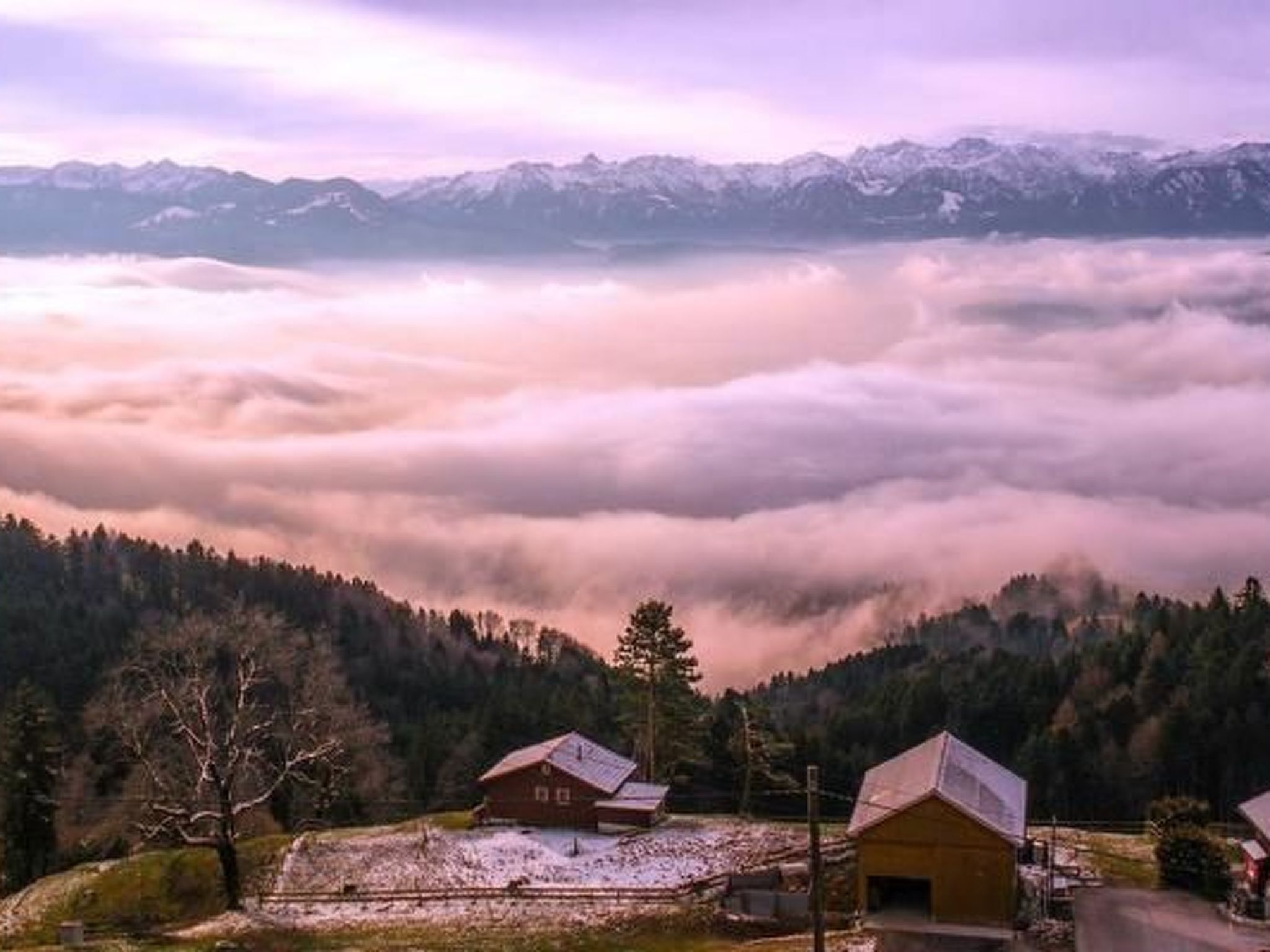 A mountain village with traditional wooden houses, a road, and a valley below.
