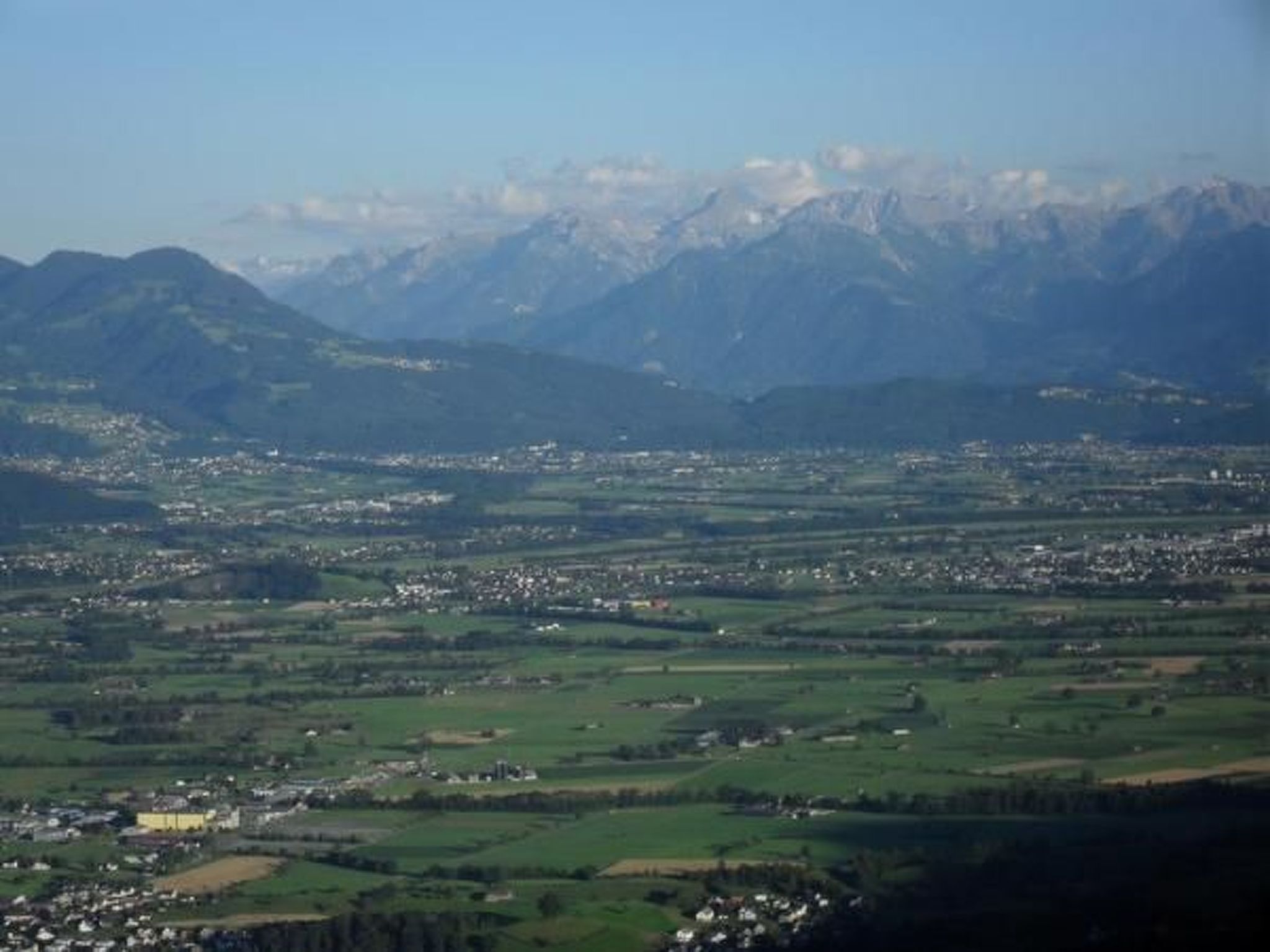 A panoramic view of a valley with a town in the foreground and mountains in the background.