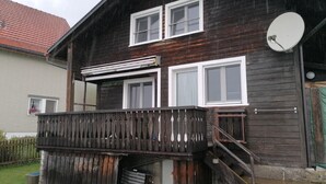 Une maison en bois à deux étages, dotée d’un balcon, d’une antenne parabolique et d’une porte de garage visible.