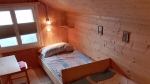 Une petite cabane en bois avec un lit simple, un bureau et une fenêtre.