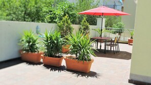 Ein Terrassenbereich mit Terrakotta-Pflanzgefäßen mit Grünpflanzen, einem roten Sonnenschirm und Gartenmöbeln.